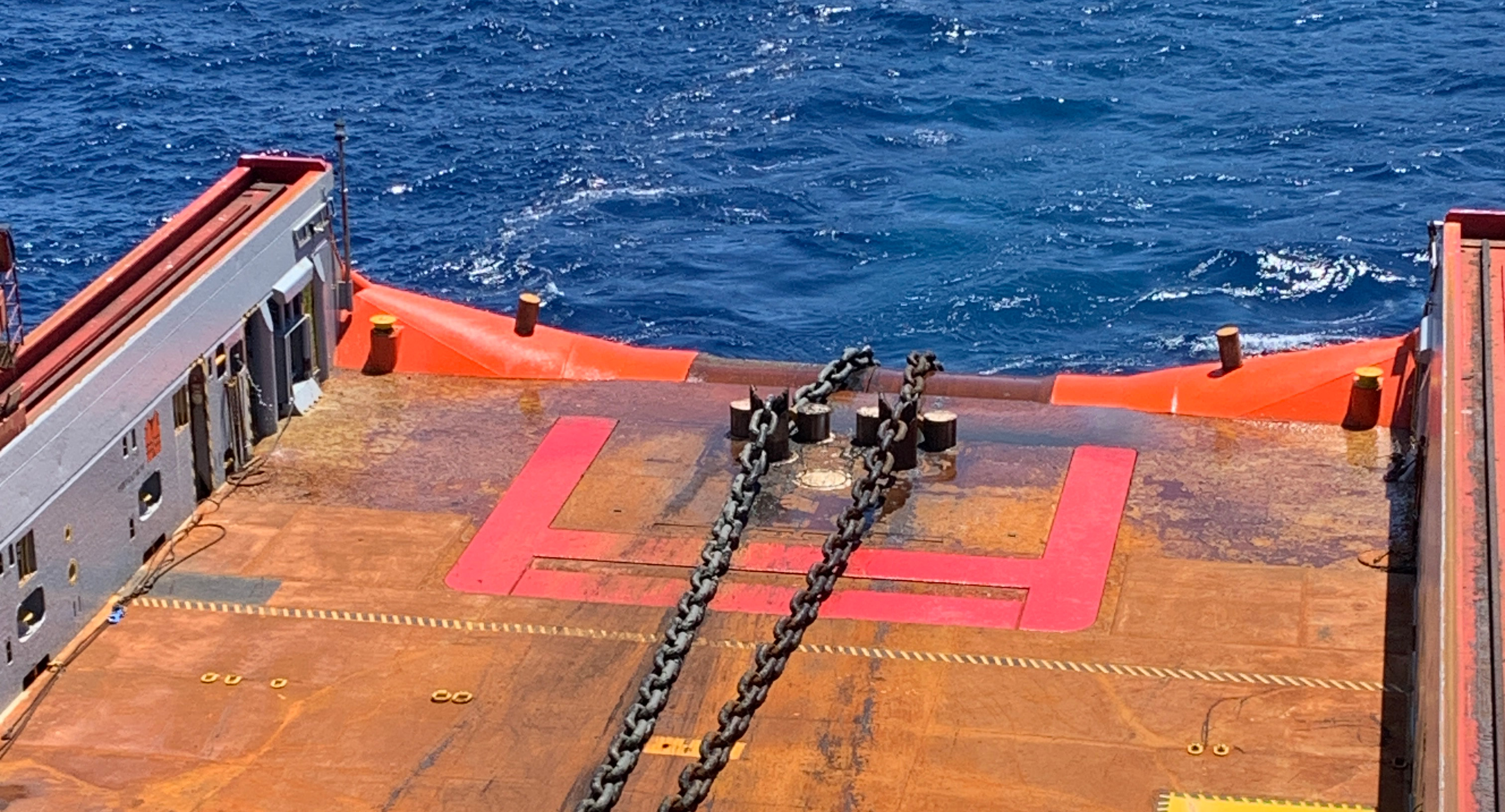 View from an Anchor Handling Vessel's deck, which is being used by Intermoor for a mooring line repair job on an FPSO, with a large chain extending toward the deep blue ocean. 