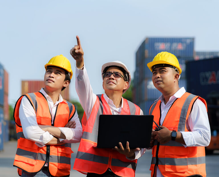Asian foreman holding laptop and explaining the various operations in the container depot terminal to worker.